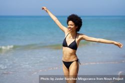 Happy woman walking on shore in bikini with outstretched arms 5qGXJb