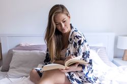 Woman in robe sitting on bed and reading a book