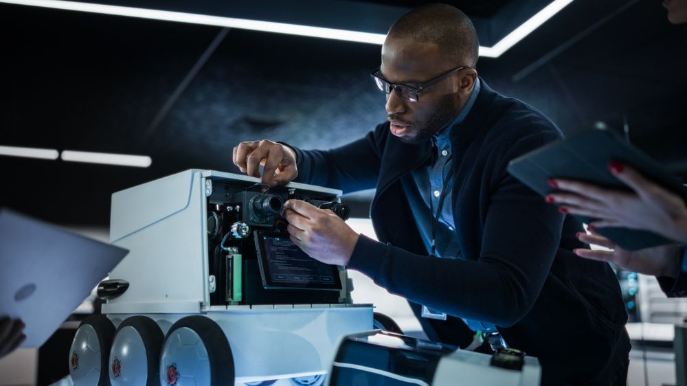 Portrait of an Engineer Using a Screwdriver While Developing a Remotely Controlled Delivery Robot. Black Specialist Working in High Tech Research Laboratory with Modern Equipment