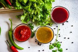 Top view of three traditional Georgian sauces tomato satsebeli, yellow and red tkemali with ingredients on stone background