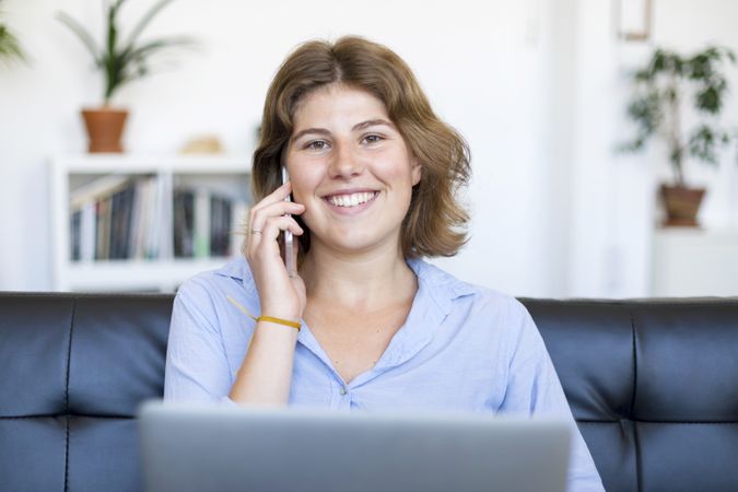 Female entrepreneur sitting on sofa at home using a laptop and chatting on phone