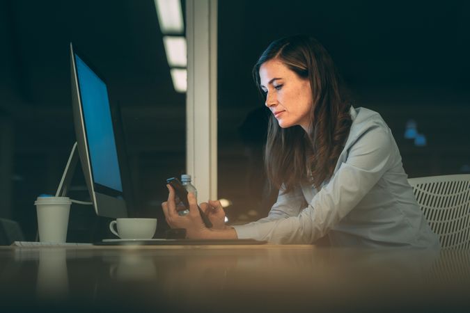 Woman entrepreneur working late night in office checking her cell phone