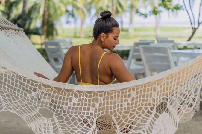 Joyful woman in bikini resting in hummock on beach