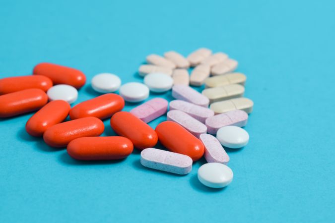Variety of pIlls in heart shape on blue table with copy space