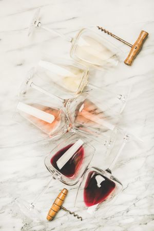 Glasses of wine laying on marble background with corkscrew
