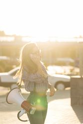 Woman standing outside speaking on phone with megaphone dressed in checkered shirt