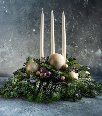Side view of purple and gold Christmas centerpiece in pine branch on table
