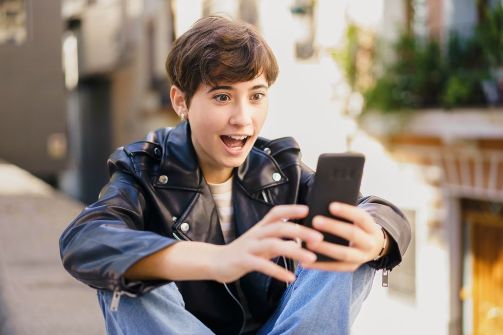 A cheerful young person is happily engaging with their smartphone in a bustling urban environment
