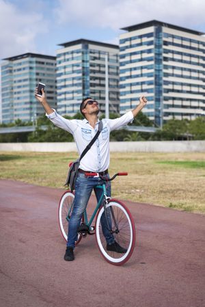 Male with colorful bicycle with phone and outstretched arms on city bike path, vertical