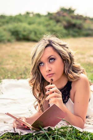 Romantic woman with a diary thinking lying down outdoors