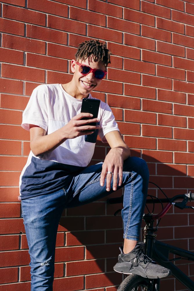 Young happy Black male browsing smartphone on bike