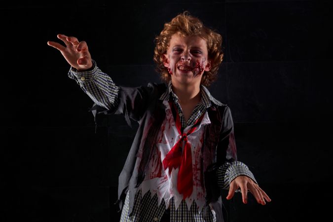 Child disguised as a zombie with blood and glitter with arms raised walking with an expression of anger
