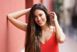 A smiling woman with long hair in a vibrant red dress posing gracefully outdoors