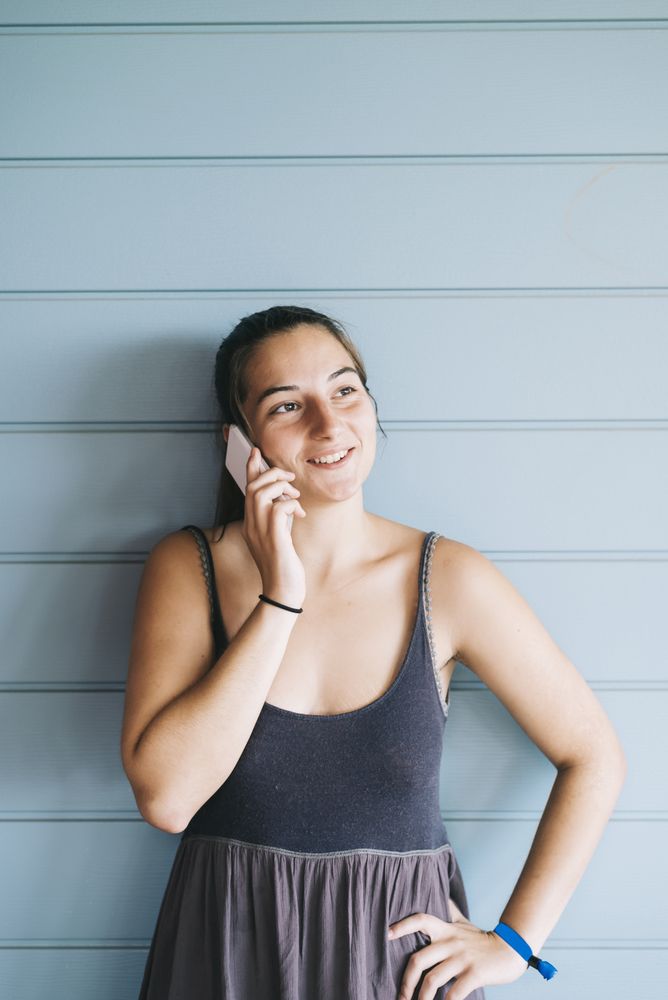 Young adult female in summer dress talking on cell phone while leaning against wood paneled wall