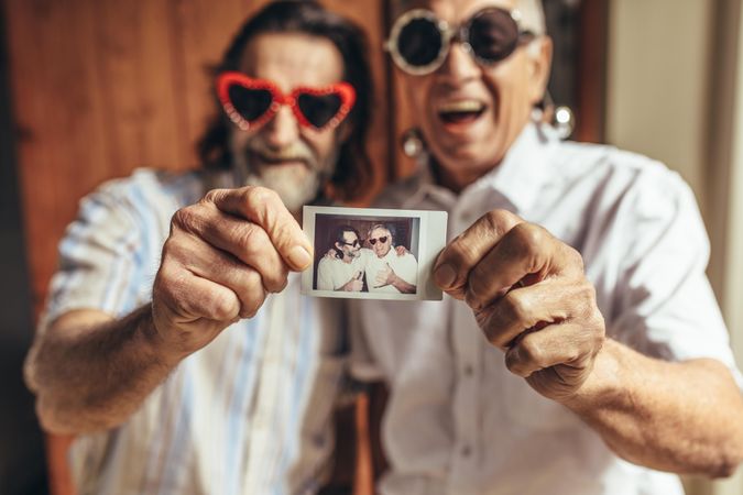 Two older male friends with party sunglasses showing their picture