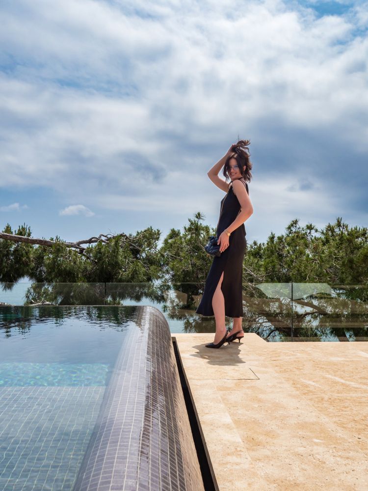 Female in a chic dress elegantly poses near the pool at a luxurious villa
