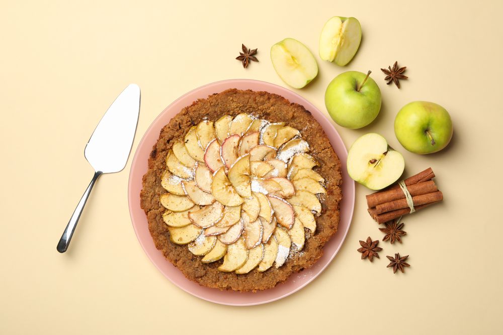 Composition with apple pie and ingredients on beige background, top view