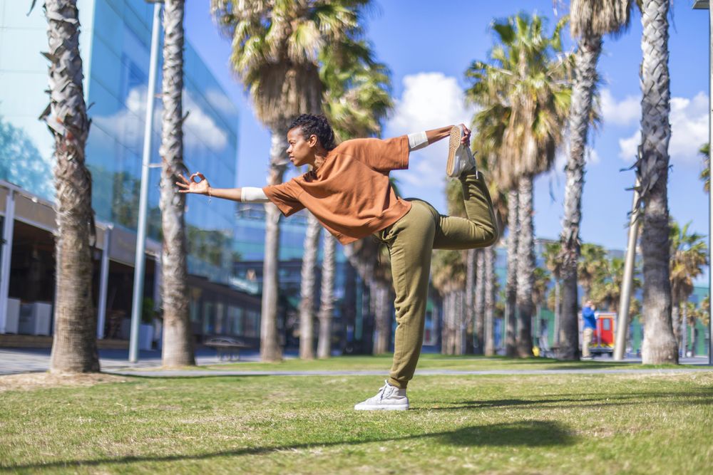 Black female stretching full body under the palms in a promenade