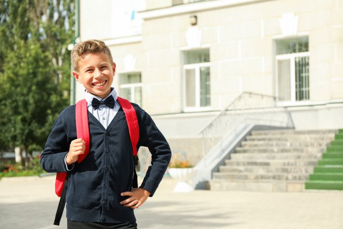Boy with backpack against school building, space for text