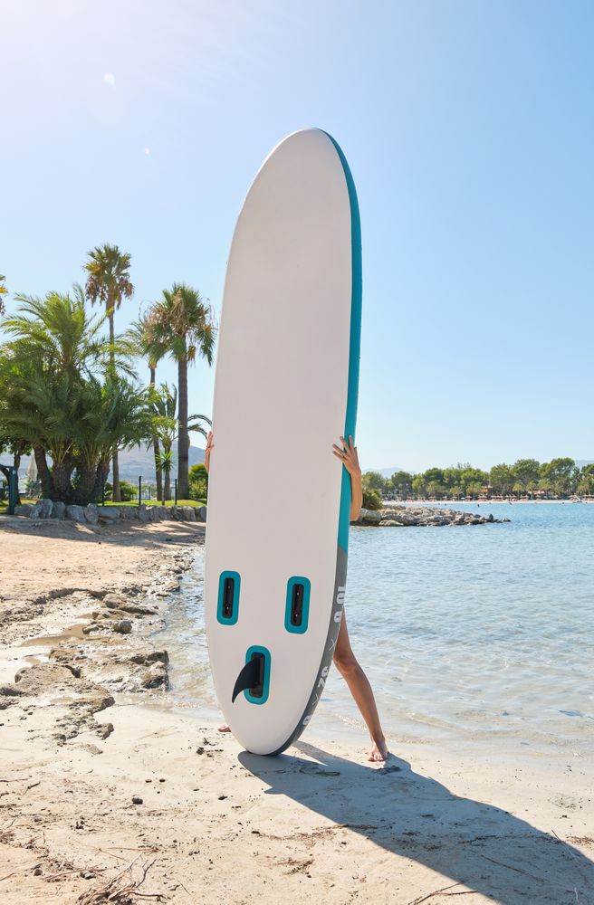 Anonymous person carrying paddleboard on coast