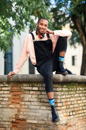 Male sitting with one leg up on brick wall in city