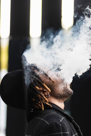 Black man exhaling cloud of smoke on street