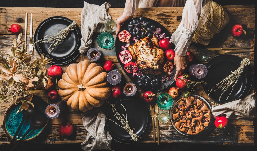 Thanksgiving party table setting for gathering with woman serving roast chicken