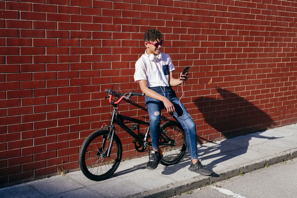 Young happy Black male browsing smartphone on bike