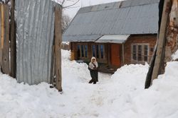 Person standing on snow covered ground beside a house in Himalayan Kashmir, India bDM9E0