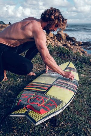 Male surfer sitting on squat covering surfboard with wax