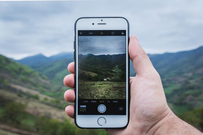 Crop hand taking picture of hilly countryside
