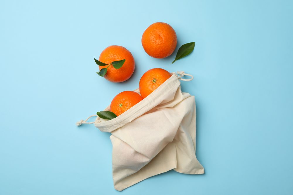 Cotton bag with ripe mandarins on blue background