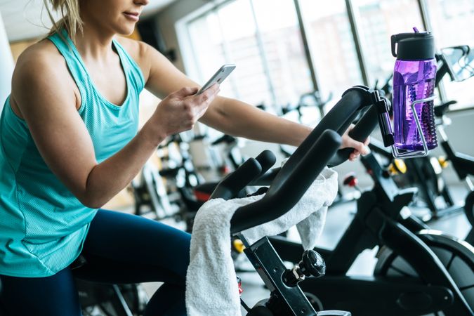 Woman with smartphone and towel and water on exercise machine