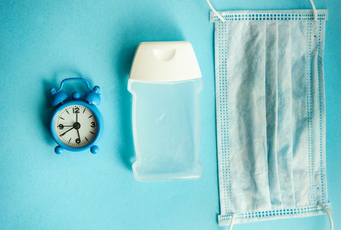 Clock, hand sanitizer and facemask on blue pastel background