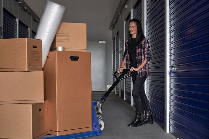 Happy woman using pallet truck to move carton boxes