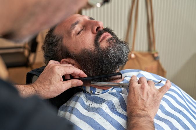 Crop barber trimming beard of male hipster