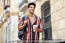 Male in striped shirt walking through the streets of Granada, Spain with coffee bxAGGa