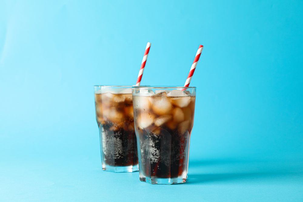 Glasses with cold cola and tubule on blue background, space for text