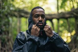 Man putting on the hood of his raincoat in the forest