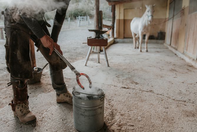 Blacksmith forging horseshoe near stable