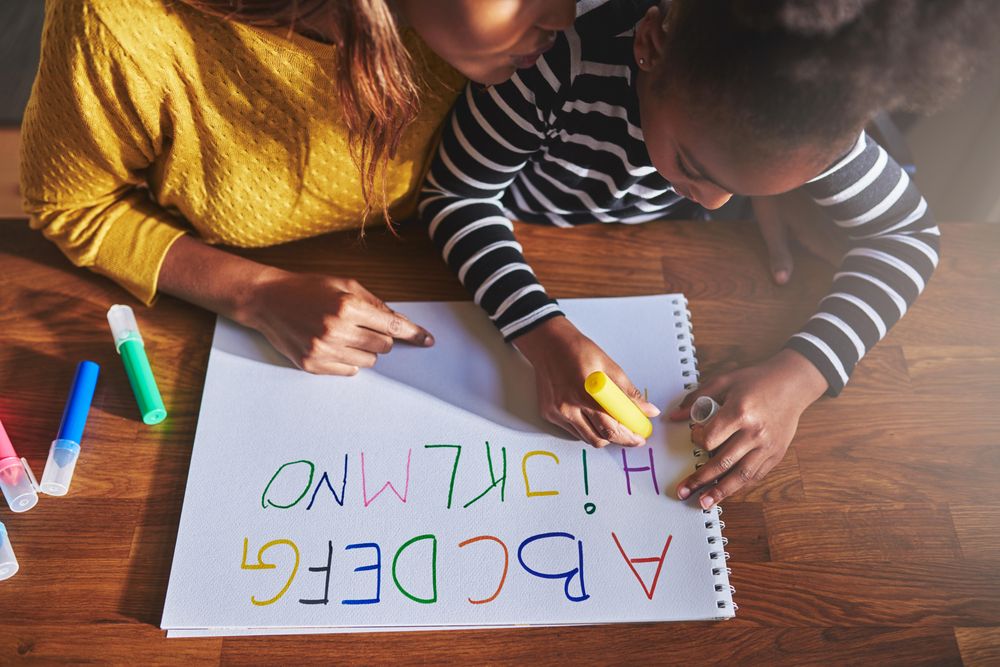 Top view of Black mother and daughter writing the alphabet at home