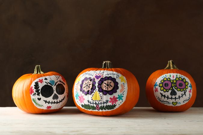 Pumpkins with catrina skull makeup on brown background
