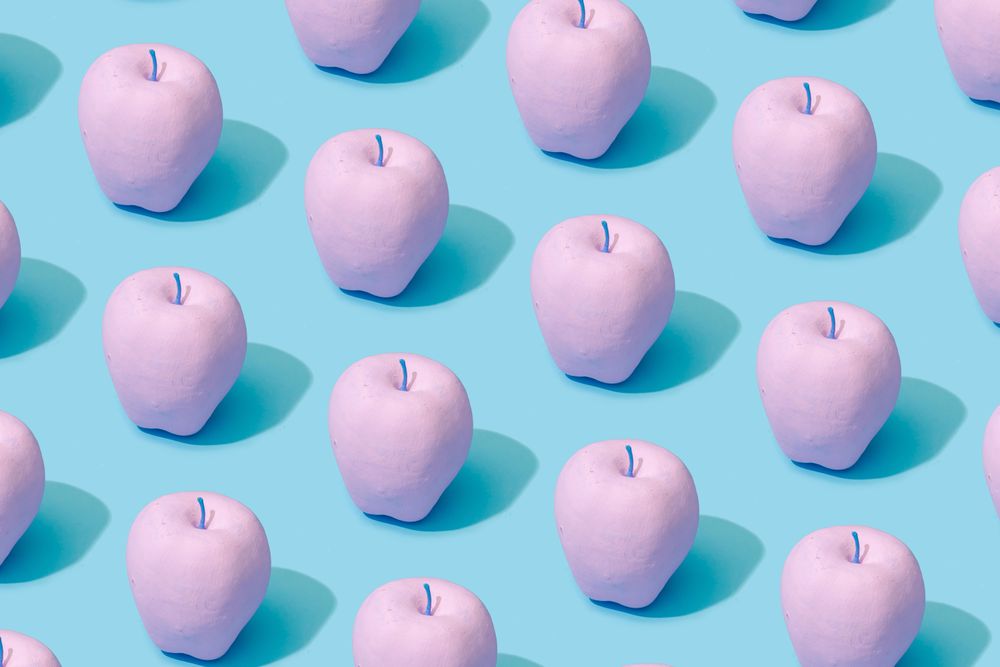 Pattern composition of pink painted apples on pastel blue background