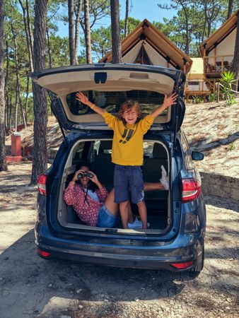 Mother and son exploring campsite while sitting in car trunk