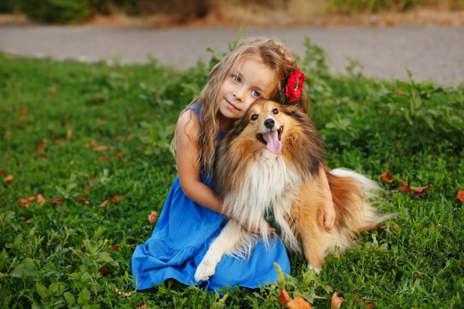 Adorable little girl in blue dress playing with pet dog in the grass