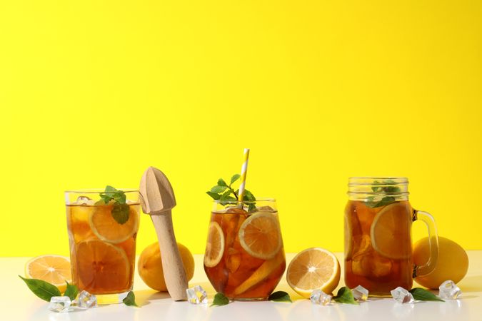 Cold tea with orange slices and mint leaves on a yellow background