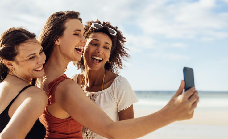 Three women friends enjoying selfie at the beach