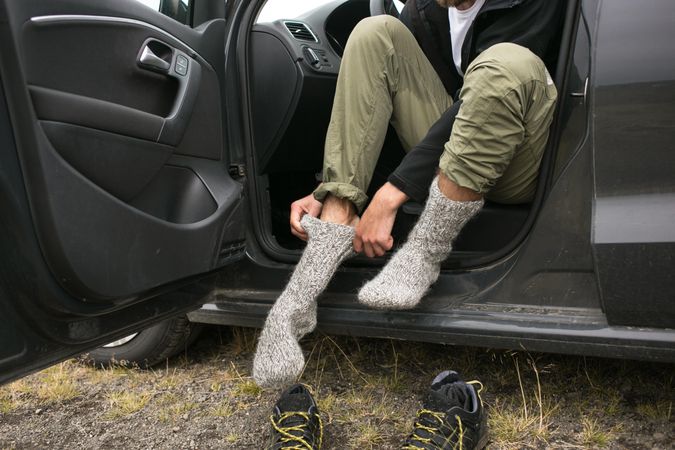Man sitting on car putting on thermal socks
