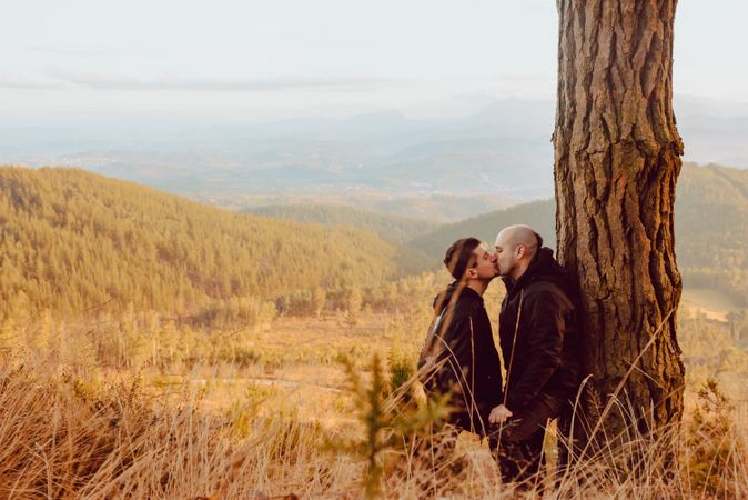 Smiling men hugging near tree in forest on hill