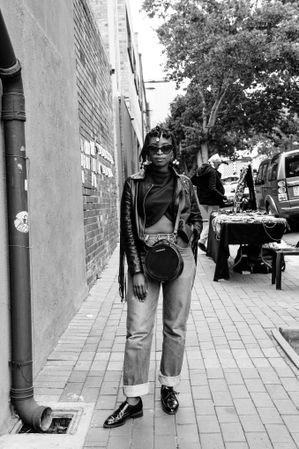 Young Black woman with jeans and purse standing looking at camera on sidewalk